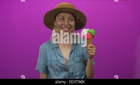 La donna tiene in studio un vivace cono gelato triplo con un ampio grin mentre presenta il dessert estivo: Gioia. Foto Stock