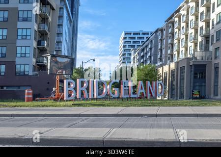 Calgary, Alberta, Canada. 5 giugno 2025. L'audace insegna BRIDGELAND, con moderni edifici di appartamenti sullo sfondo, accoglie residenti e visitatori in una Foto Stock