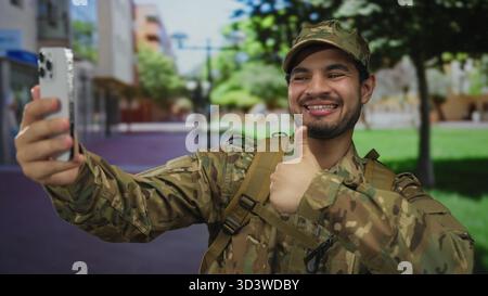 Uomo in uniforme mimetica con zaino, scatta selfie con lo smartphone in città; servizio Pride. Foto Stock