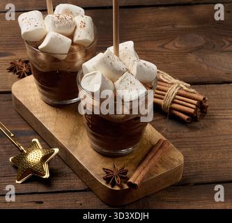 Due bicchieri di cioccolata calda con soffici marshmallow e una cannuccia su un vassoio di legno Un accogliente drink invernale su uno sfondo scuro. Foto Stock