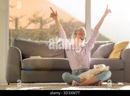 Una giovane donna felicissima seduta a terra con un cane westie terrier in grembo che danzava e ascoltava musica Foto Stock