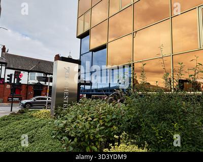 Manchester, Regno Unito - 30 settembre 2025: Moderno edificio in vetro riflettente a Manchester con paesaggio e scena di strada. Foto Stock