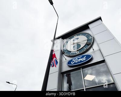 Manchester, Regno Unito - 30 settembre 2025: Orologio e marchio Ford su un elegante negozio di Manchester con bandiera e ambientazione urbana. Foto Stock