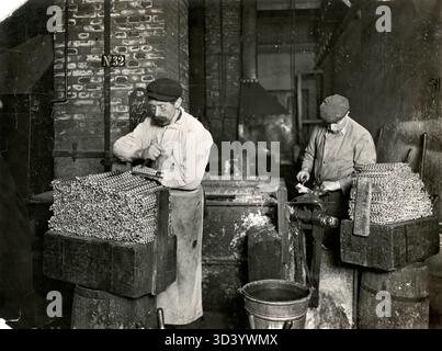 Alla Royal Artillery Factory di Hembrug, Paesi Bassi, vengono lanciati proiettili per riempire granate. Il processo prevede il versamento di piombo fuso negli stampi, con i lavoratori che tagliano e modellano i proiettili. Foto, 1912. Foto Stock