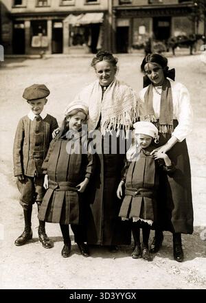 Una rappresentazione della tipica moda inglese per bambini del 1915. Le ragazze indossano abiti a pieghe, mentre il ragazzo è vestito con un Plus-quattro, calze lunghe, una giacca con colletto bianco e un berretto. Foto Stock