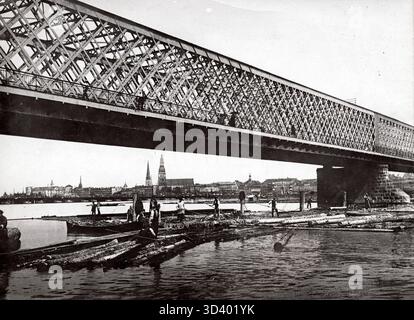 Una veduta di riga, Russia, nel 1915, mostra il ponte ferroviario di ferro sul fiume Dvina occidentale/Duna, con uomini che trasportano tronchi trasportati dal fiume. Foto Stock