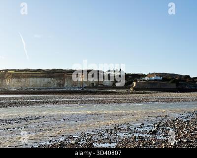 Una tranquilla scena costiera con case sulla scogliera lungo la riva sotto un cielo azzurro. Foto Stock