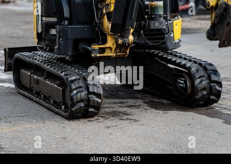 Escavatore compatto con cingoli in gomma parcheggiati su una superficie asfaltata, che rappresenta i moderni macchinari per l'edilizia, le attrezzature per l'ingegneria industriale e il terreno Foto Stock