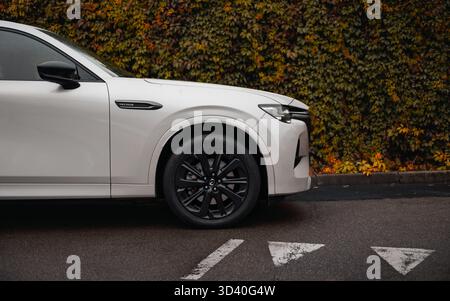 Parte anteriore del SUV argentato vicino al muro dell'arbusto. Vista laterale del crossover giapponese Mazda CX-60 parcheggiato dalla siepe autunnale. Foto Stock