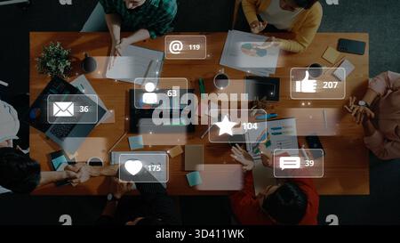 Vista aerea di uno spazio di lavoro collaborativo che mostra le persone impegnate in discussioni con icone dei social media digitali e metriche che evidenziano la comunicazione Foto Stock