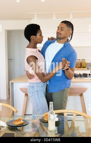 Danzare diverse coppie che si tengono per mano nella moderna cucina casalinga, con tavolo da pranzo in vetro e panini Foto Stock