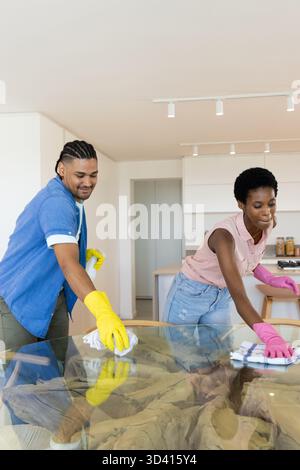 Diverse coppie che puliscono il tavolo da pranzo in vetro nella moderna sala da pranzo, con guanti e panni di gomma Foto Stock