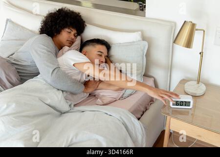 Coccolante coppia di uomini in una moderna camera da letto con sveglia digitale Foto Stock