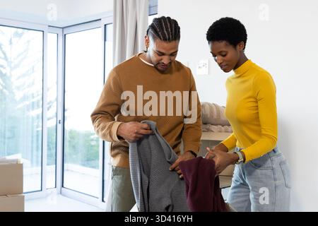 Coppie diverse che esaminano maglioni in maglia grigia e Bordeaux nel nuovo salotto di casa, con scatole mobili Foto Stock