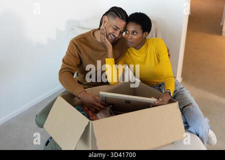 Disimballaggio di diverse coppie, smistamento di abiti e immagine incorniciata sul divano del soggiorno, con scatola di cartone Foto Stock