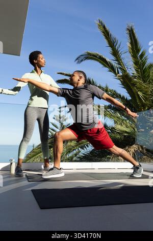 Diversi partner di allenamento che praticano yoga sulla terrazza all'aperto, con due tappetini neri e ringhiera in vetro Foto Stock