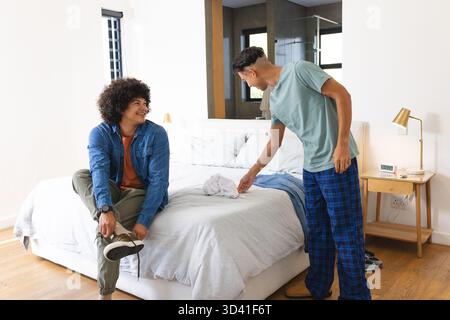 Diversi amici maschili si vestono in una camera luminosa, con letto queen size e sneakers bianche Foto Stock