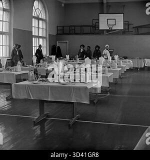 Una foto d'archivio del 1984 mostra una mensa per i delegati di una conferenza cittadina presso la Casa della Cultura Artyom (DK) a Sloviansk, RSS Ucraina. La palestra, con il suo canestro da basket e le finestre ad arco, è stata temporaneamente convertita in una sala da pranzo. I tavoli lunghi sono preparati con pasti, tra cui piatti, bicchieri e grandi bottiglie di latte in vetro. Questa scena cattura il catering per un evento ufficiale sovietico. Questo è un momento della vita quotidiana nel pacifico Donbas prima della guerra. Foto Stock
