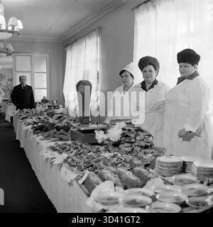 Una foto d'archivio del 1984 mostra la linea del buffet per una conferenza alla Casa della Cultura Artyom (DK) a Sloviansk, RSS Ucraina. Tre donne del personale di cucina con uniformi bianche e cappelli si posano dietro un lungo tavolo. Il tavolo è carico di una vasta gamma di antipasti freddi ("zakuski"), carni, insalate e pane, con scaglie e pile di piatti puliti pronti per i partecipanti. Questo cattura il catering per un evento ufficiale sovietico. Questo è un momento della vita quotidiana nel pacifico Donbas prima della guerra. Foto Stock