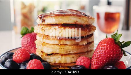 Colazione, pancake e fragole con pasto nella cucina di casa per fame, nutrizione o spuntino. Cibo, frutta e sciroppo con pasticceria biologica Foto Stock