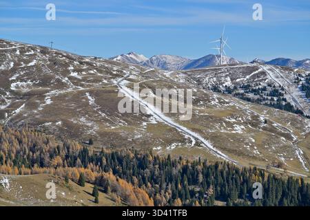Montagne innevate di Lachtal con turbine eoliche, stazioni sciistiche e larici dorati sotto un cielo blu. Foto Stock