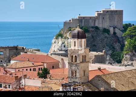 Vista iconica di Dubrovnik, Croazia. Fort Lovrijenac si erge sul Mare Adriatico, con uno storico campanile e tetti in terracotta in primo piano Foto Stock