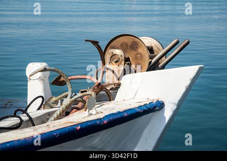 Vecchia barca da pesca in legno con bobine meccaniche d'epoca ancorata su un mare blu calmo Foto Stock