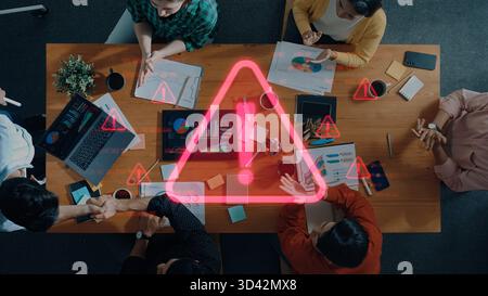 Un gruppo di professionisti partecipa a una riunione collaborativa che analizza i dati con grafici. Una sovrapposizione di un'icona di avvertenza mette in evidenza i potenziali rischi in Foto Stock
