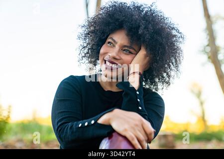 Giovane donna nera sorridente, che guarda lontano con un'espressione premurosa e felice Foto Stock