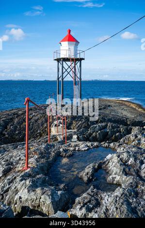 Kvalen fyr, un faro rosso e bianco si erge su un terreno roccioso vicino al mare, con un sentiero che conduce ad esso, tiro verticale, Haugesund, Norvegia Foto Stock