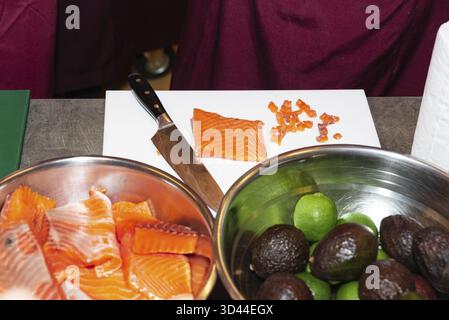 Cibo, salmone affettato su un tagliere accanto a ciotole di pesce crudo, avocado e limes, pronto per la preparazione di pesce fresco Foto Stock