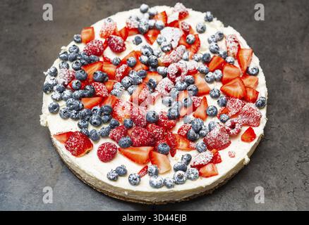 Cibo, classica cheesecake ricoperta di fragole, lamponi e mirtilli, spolverata con zucchero a velo per un dessert festoso e delizioso Foto Stock