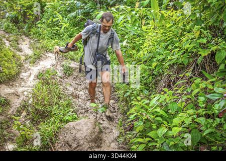 Uomo che cammina nel fango profondo su un sentiero da Maroantsetra a Antalaha Foto Stock