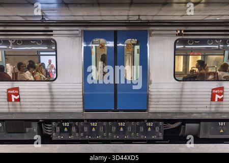 Vista laterale di un'auto della metropolitana di Lisbona ferma in una stazione. I passeggeri sono visibili attraverso i finestrini, accanto alle doppie porte blu. Lisbona, Portuga Foto Stock
