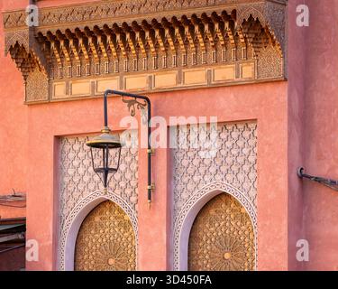 Architettura marocchina nella medina di Marrakech, caratterizzata da porte ad arco intagliate, motivi geometrici islamici e una lanterna sotto ornati dettagli in legno. Foto Stock