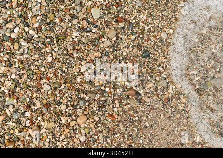 Colorati ciottoli di mare sparsi lungo la costa, con le onde che si lavano delicatamente sopra di loro. sassolini colorati e ghiaia fine ai margini del mare. Gentile Foto Stock