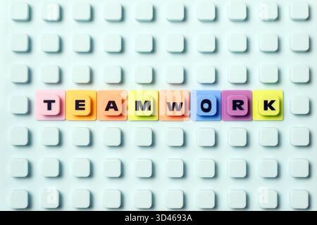La parola "LAVORO DI SQUADRA" è stata pronunciata in piastrelle di plastica colorate su una superficie blu di mattoni, simboleggiando la collaborazione, la strategia e il suc aziendale Foto Stock