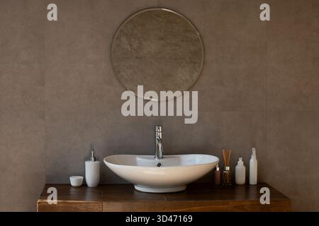Moderno e lussuoso bagno interno con elegante lavandino e specchio rotondo in un elegante appartamento Foto Stock