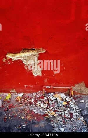 Pareti in gesso rosso danneggiate con mattoni esposti e detriti sparsi sul terreno in un ambiente urbano Foto Stock