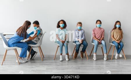 Diversi bambini ricevono vaccinazioni Covid-19 in un ambiente sanitario Foto Stock