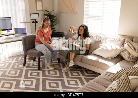 Diverse colleghe di sesso femminile sedute in ufficio a casa a discutere di documenti stampati, con un notebook Foto Stock