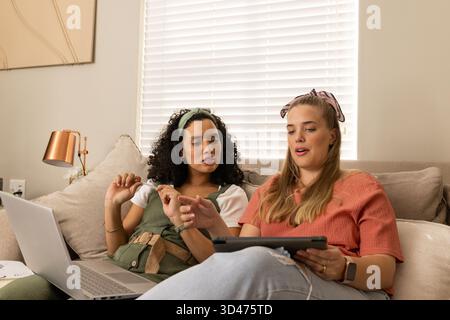 Collaborare con diverse amiche con tablet e computer portatile sul divano del soggiorno, con lampada in rame Foto Stock