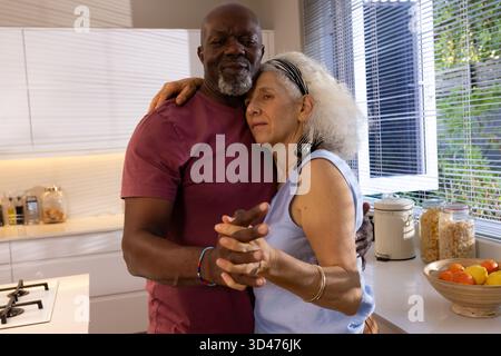 Ballare diverse coppie anziane tenendosi per mano in una cucina moderna, con cesto di frutta in legno Foto Stock
