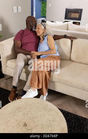 Baciare la coppia senior che si piega l'una all'altra nel soggiorno, con divano a righe e caminetto Foto Stock