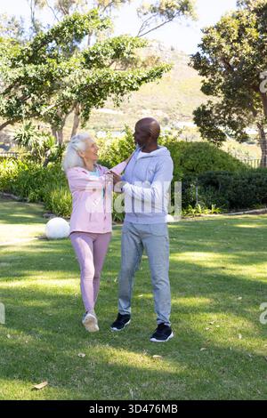 Ballare diverse coppie anziane tenendosi per mano su un prato erboso in giardino, con sfere bianche da giardino Foto Stock