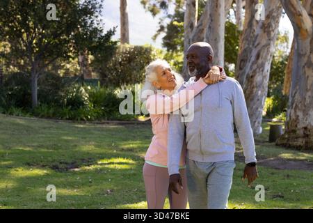 Cammina per diverse coppie senior che si abbracciano su prato erboso nel parco, con smartwatch visibile Foto Stock