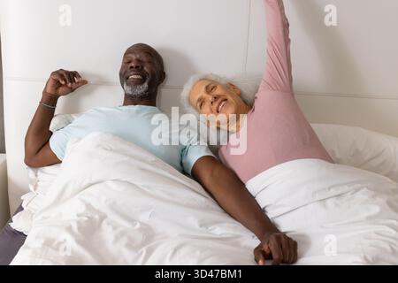 Allungando diverse coppie sorridenti, tenendosi per mano e sdraiati a letto, con lenzuola bianche e testiera Foto Stock