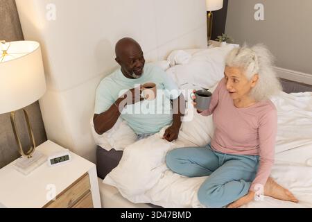 Sorseggiando un caffè diverse coppie senior sedute insieme sul letto in una camera moderna, con tazze in ceramica Foto Stock