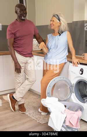 Una coppia di anziani con diverse mani in lavanderia, con cestino per la lavanderia e lavatrice aperta Foto Stock