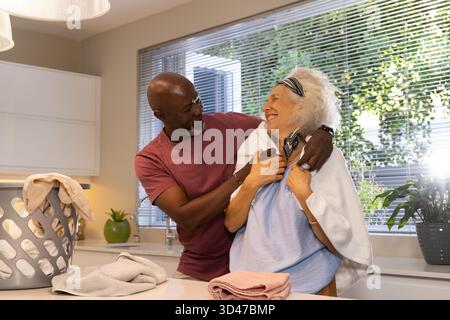 Una coppia di anziani ridendo, lavanderia pieghevole in una cucina moderna, con cestino per lavanderia e vasetti Foto Stock